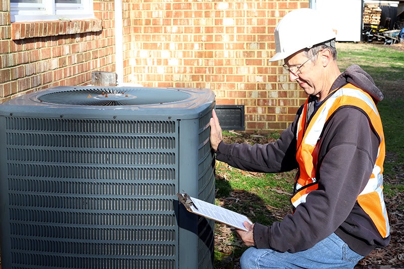 Home inspection of central air unit by a maintenance worker.